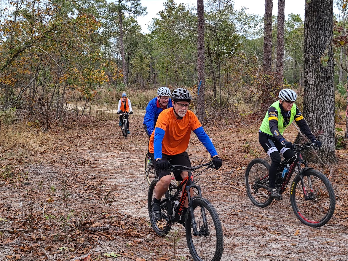4 Bikers with bright colored clothes and helmets riding down a path at Clemson Lloyd property