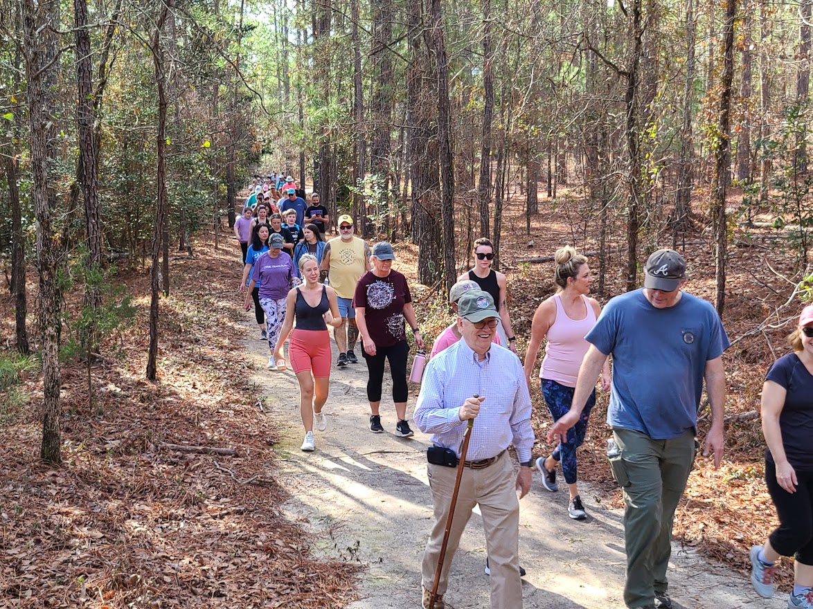first-day-hike-goodale A parade of people walking the Goodale state park Nature trail on The First Day Hike. One person with a walking stick and people in comfortable clothing smiling